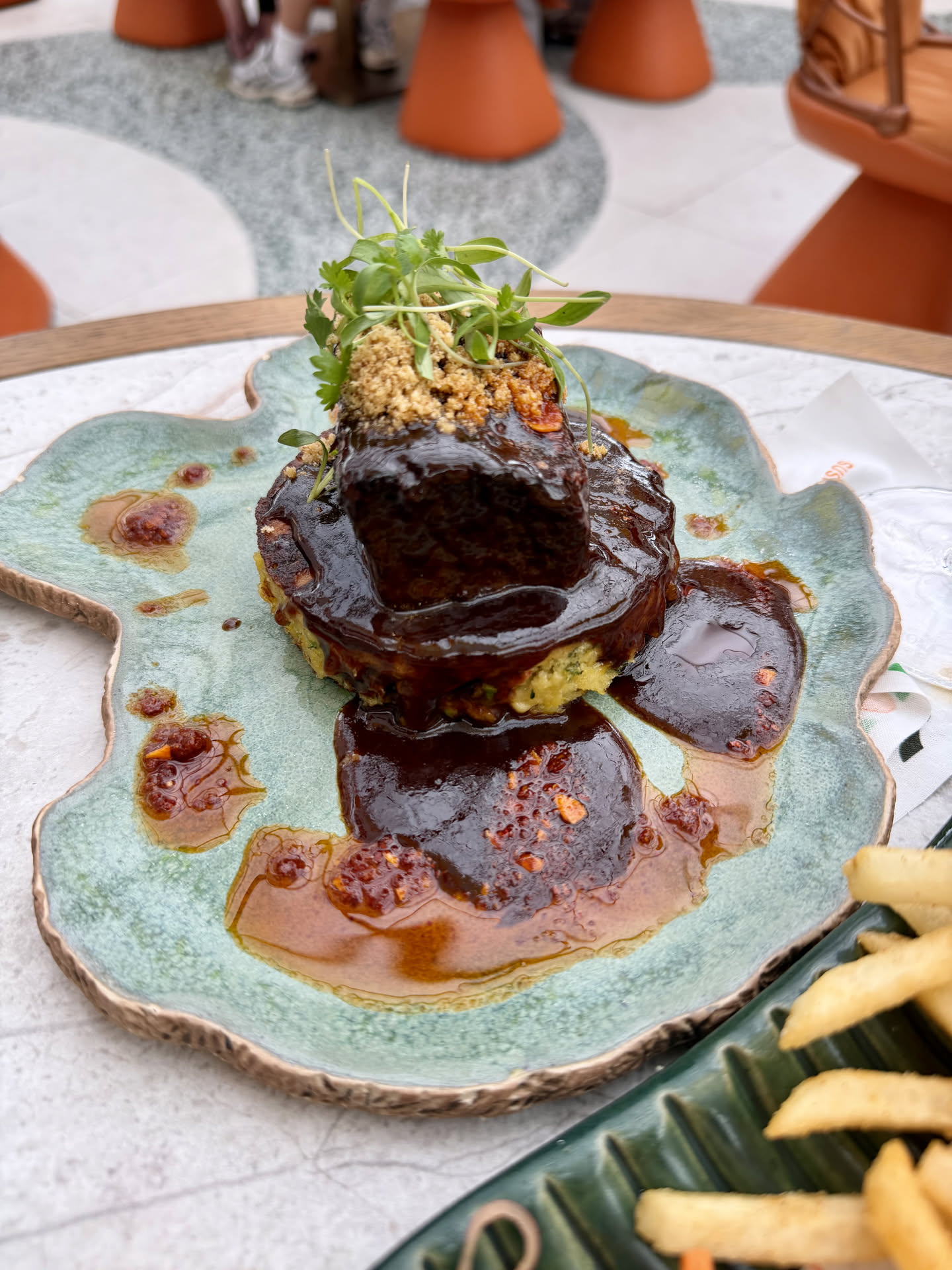 Braised short rib with dark glaze over a corn pancake on a green ceramic plate