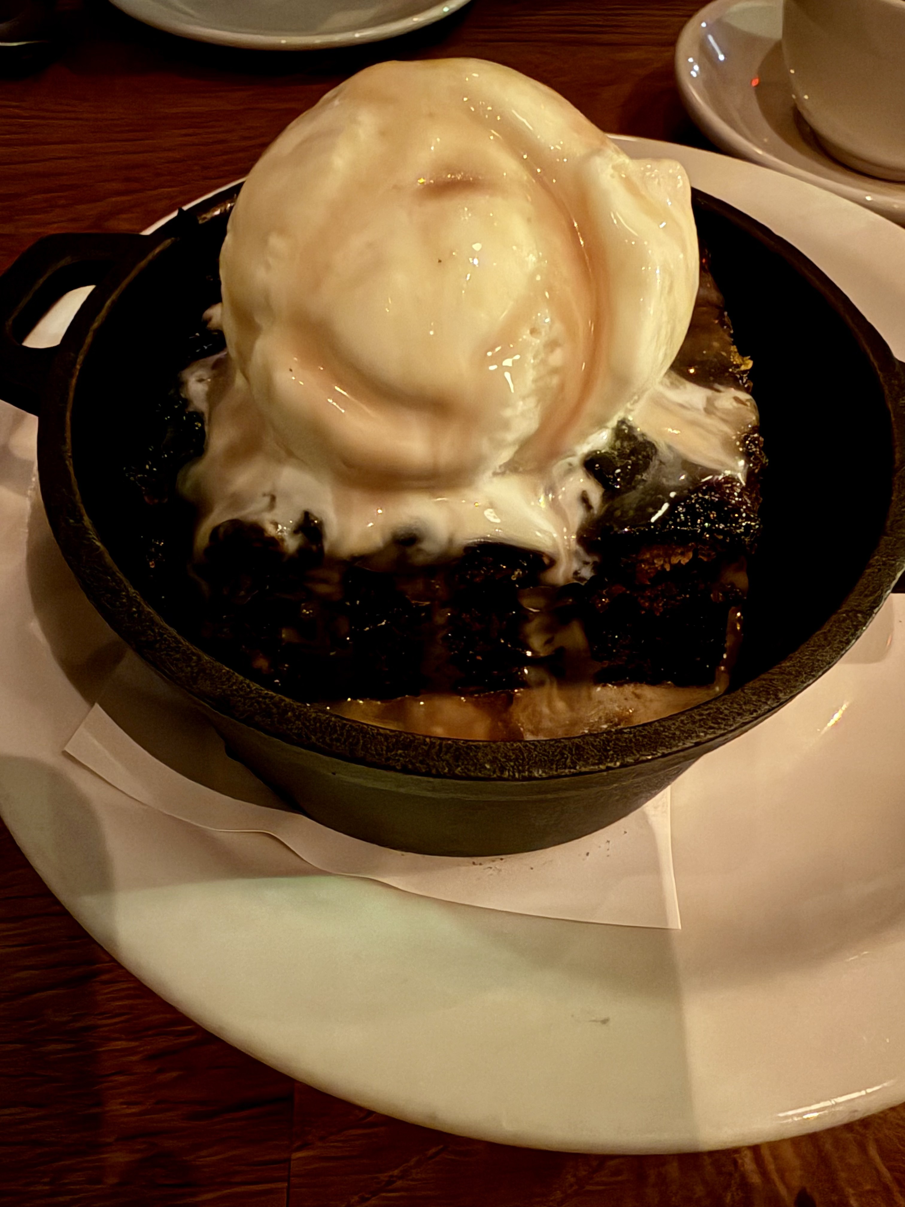 Sticky date pudding in a cast iron dish topped with a large scoop of vanilla ice cream and toffee sauce